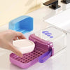 A hand holds a pink silicone leakproof travel container with a perforated tray and a clear lid on a white surface.