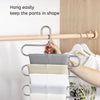 A multi-layer stainless steel clothes rack hanging on a wooden rod, holding several folded white and beige garments.