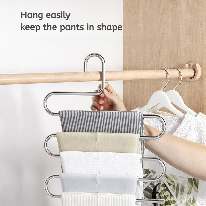 A multi-layer stainless steel clothes rack hanging on a wooden rod, holding several folded white and beige garments.