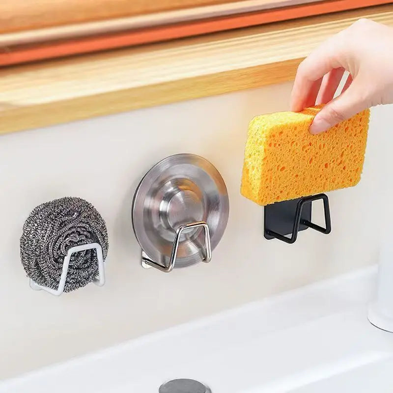 A hand is holding a yellow sponge over a stainless steel holder rack with a suction cup mounted on a white surface.