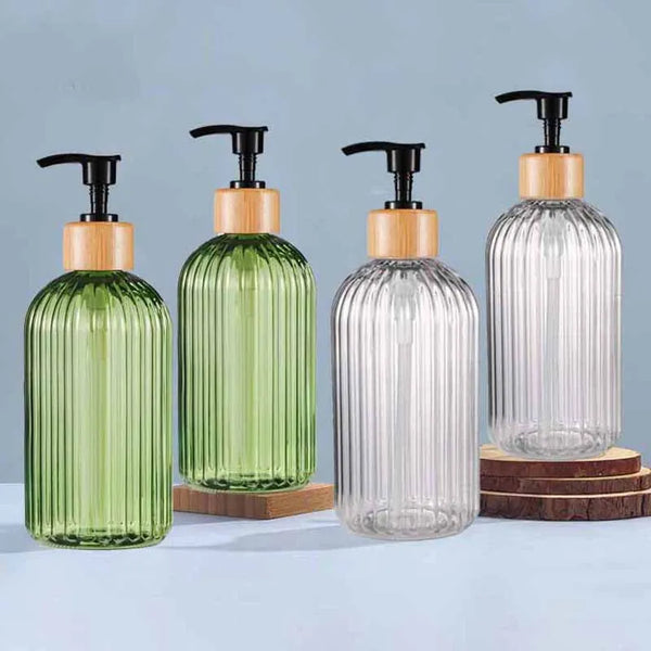 A set of four glass soap dispensers with wooden caps and black pumps in shades of green and clear.