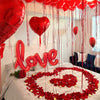 Rote herzförmige Ballonbriefe und rote Rosenblüten schmücken ein Bett für einen besonderen Anlass