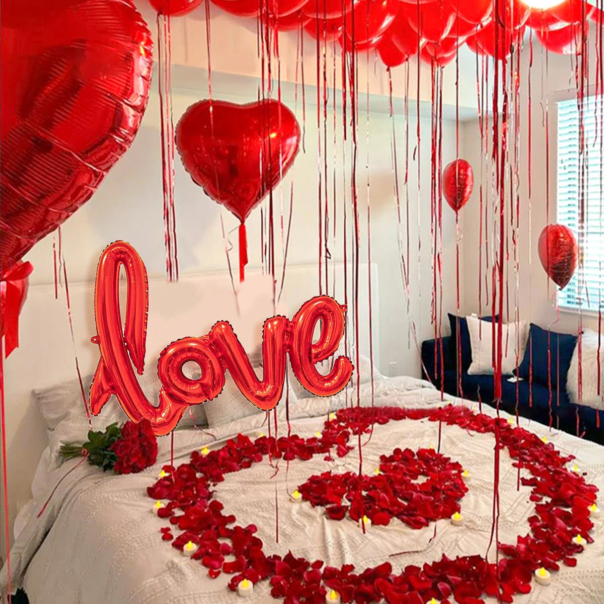 Rote herzförmige Ballonbriefe und rote Rosenblüten schmücken ein Bett für einen besonderen Anlass