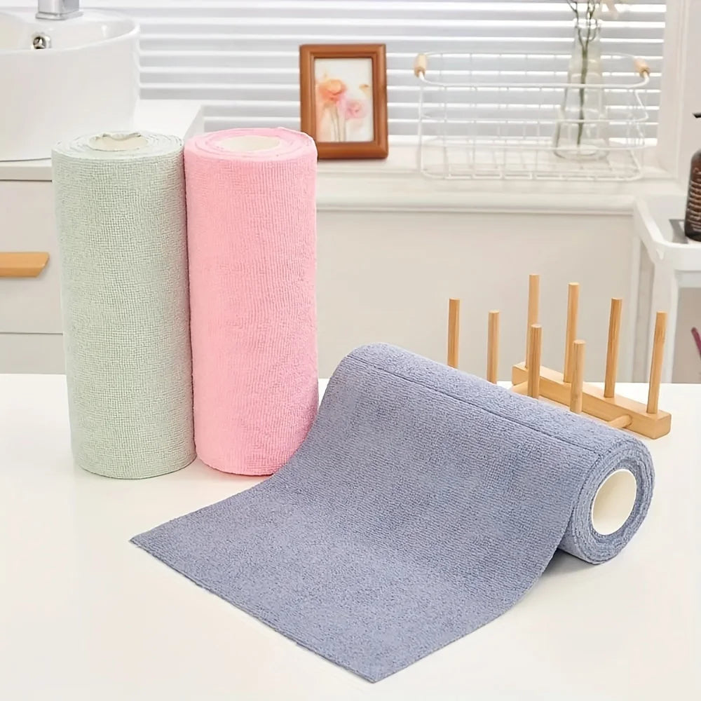A stack of pink and green reusable microfiber cleaning cloths next to a purple cloth on a white countertop.