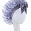 A lavender silky satin sleep bonnet tied with a bow displayed on a white mannequin head.