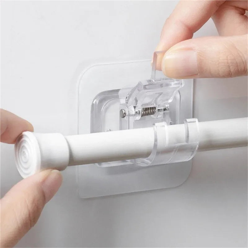 A hand is installing a clear plastic hook onto a white curtain rod using a self-adhesive set of hooks.
