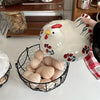 A white ceramic hen-shaped bowl is shown holding a basket full of brown eggs.