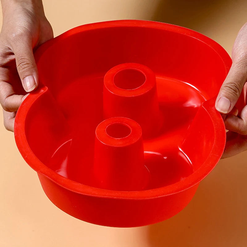 Hands holding a bright red silicone cake mold with multiple round indentations.