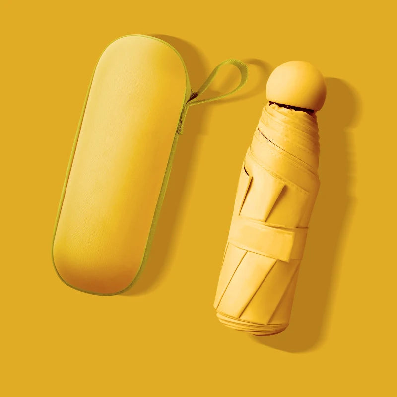 A yellow mini travel umbrella with a green strap is shown against a mustard yellow background.
