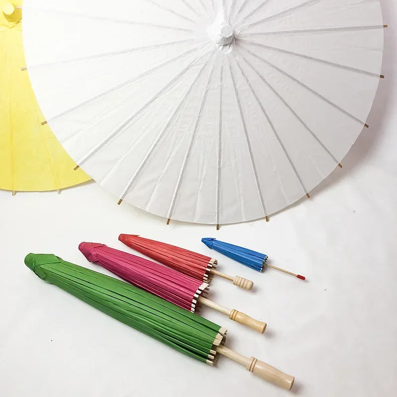 Un paraguas de papel blanco abierto junto a varios paraguas de papel coloridos.