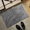 A square gray diatomite bath mat placed on a light stone surface with a black slipper nearby.