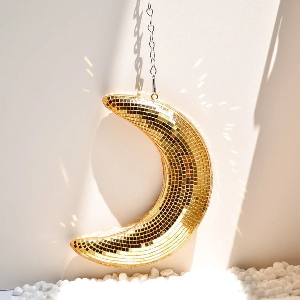 A golden, mosaic moon pendant hangs against a white wall, casting light rays.