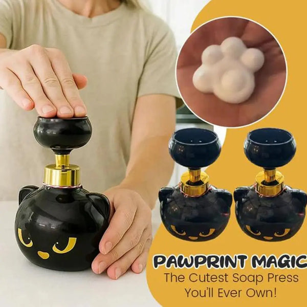 A black soap press dispenser shaped like a cat's head with gold accents, shown next to a hand and a close-up of soap foam.