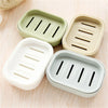 Three double layer drain soap dishes in light green, beige, and white are arranged on a wooden surface.