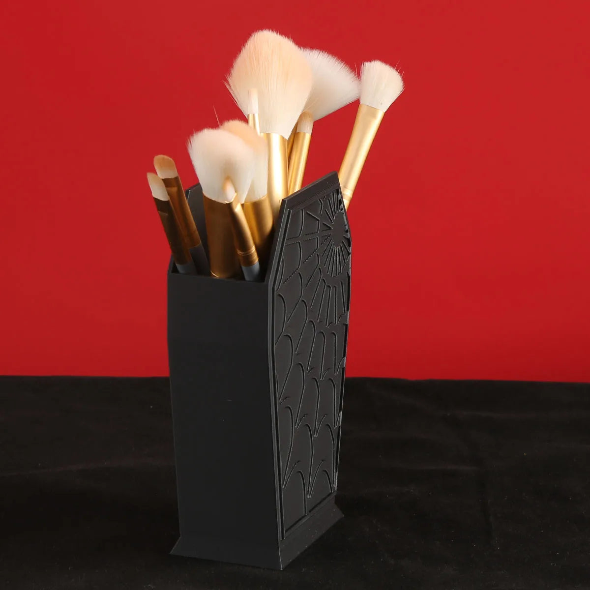 A black coffin-shaped makeup brush holder with a spider web design filled with various makeup brushes.