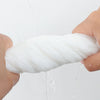 A hand is squeezing a thick white disposable facial cleansing towel, with water dripping from the towel.