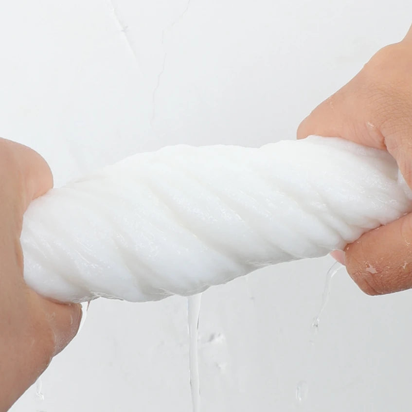 A hand is squeezing a thick white disposable facial cleansing towel, with water dripping from the towel.