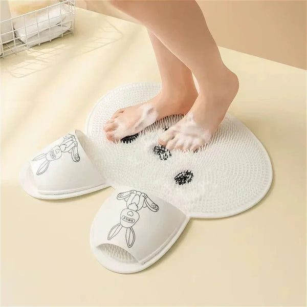 A person's feet are resting on a white silicone mat designed for foot massage and scrubbing.