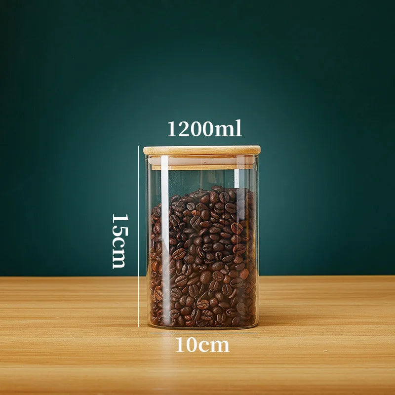 A clear glass storage canister filled with dark roasted coffee beans, sitting on a wooden surface.