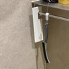 A white cleaning brush with a gray handle is mounted on a shelf, designed for crevice cleaning.