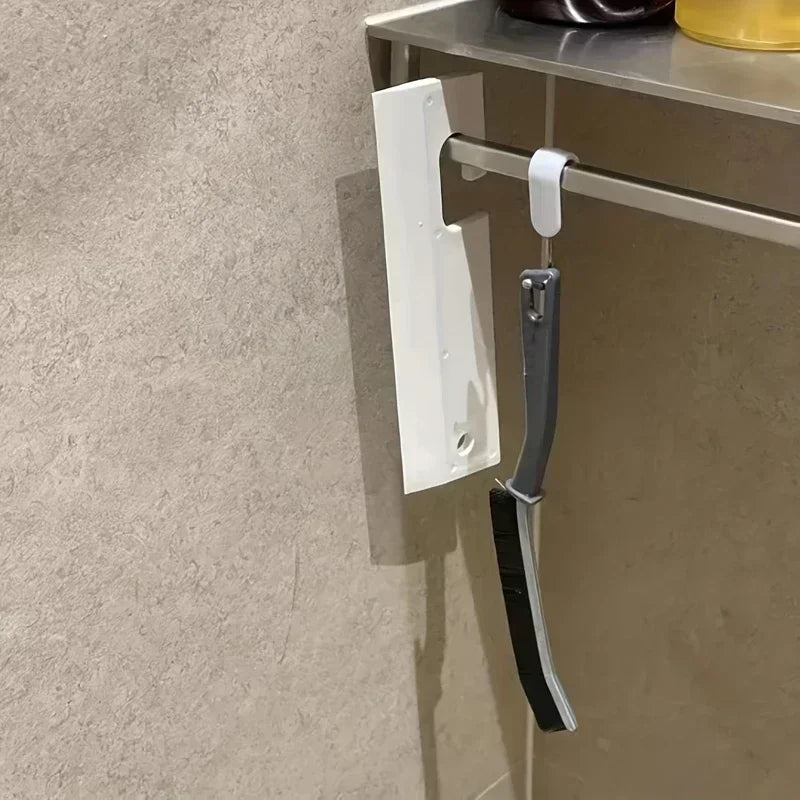 A white cleaning brush with a gray handle is mounted on a shelf, designed for crevice cleaning.