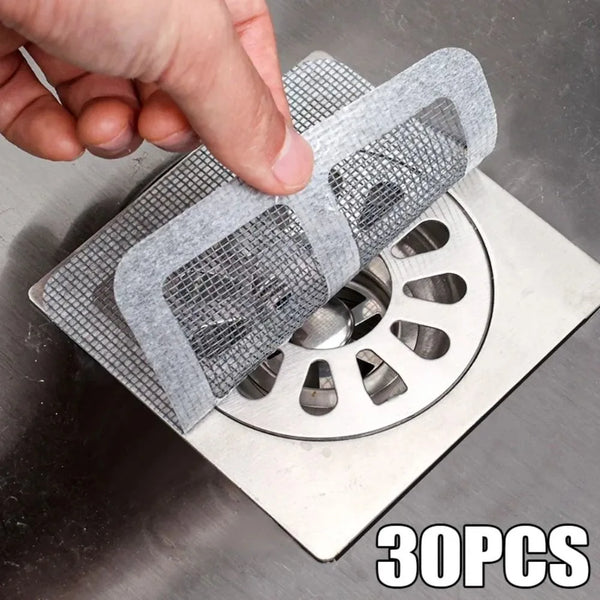 A hand is placing a disposable drain strainer sticker onto a metal drain grate.