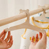 A pair of wooden clothing hangers for kids are being held up against a white curtain.