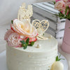 A white tiered wedding cake decorated with pink roses and a gold rhinestone Mr & Mrs topper.