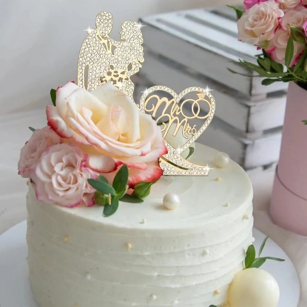A white tiered wedding cake decorated with pink roses and a gold rhinestone Mr & Mrs topper.