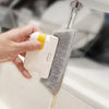 A hand is using a white cleaning brush with a yellow handle to clean a window pane.
