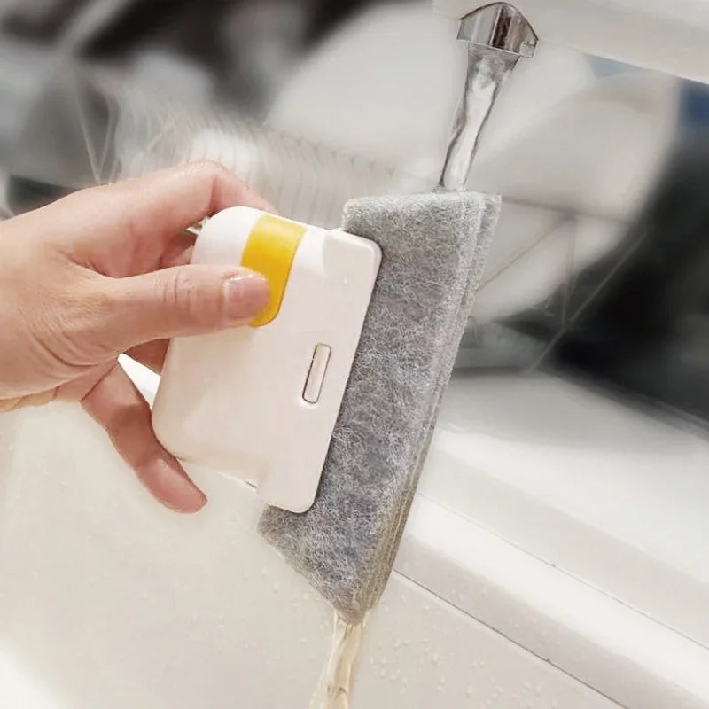 A hand is using a white cleaning brush with a yellow handle to clean a window pane.