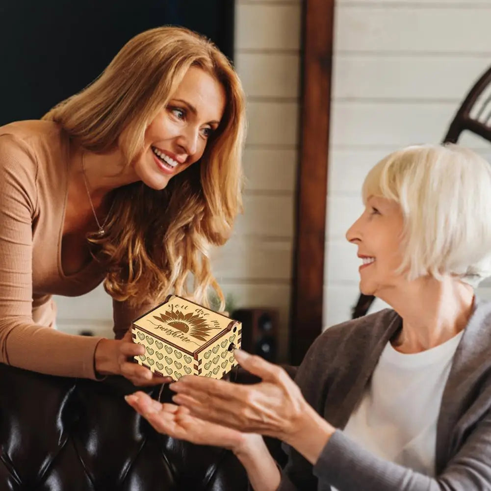 A woman is showing a mini wooden music box to another woman in a warm indoor setting.