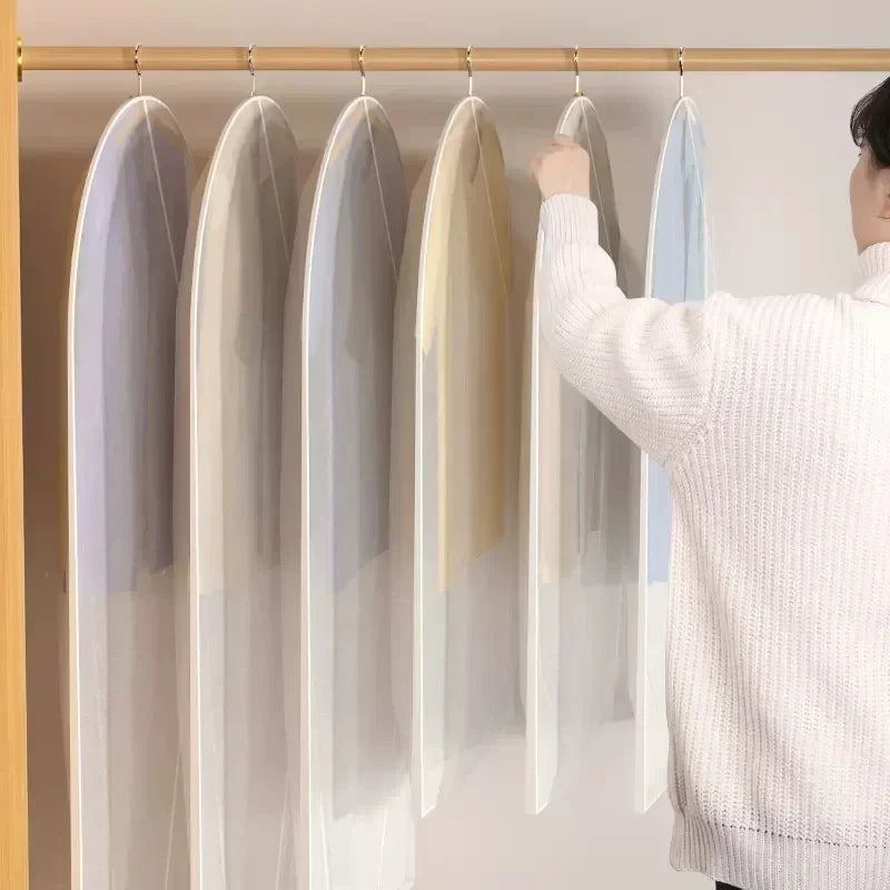 A person is hanging a sheer dust cover over a garment on a wooden rod.