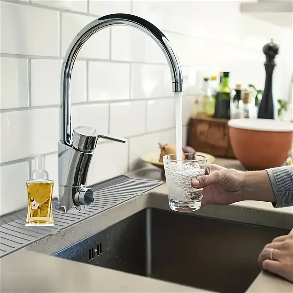 Eine Hand hält ein Glas Wasser, das durch einen modernen Küchenhahn in eine Edelstahlspüle fließt.