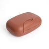 A smooth, terracotta-colored portable travel soap box with a rounded, ergonomic design.