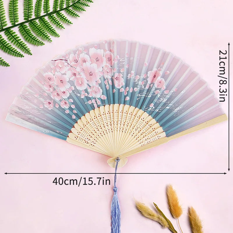 A delicate pink and blue lace fabric folding hand fan with a natural wood-colored fan and decorative floral accents.