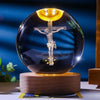 A dark glass crystal ball with a glowing crucifix inside, resting on a wooden base.