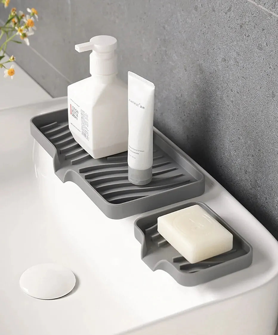 A silicone draining soap tray organizer holding a white pump bottle and a bar of soap on a white countertop.