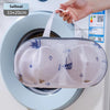 A white mesh laundry bag with blue embroidery is placed inside a washing machine drum.