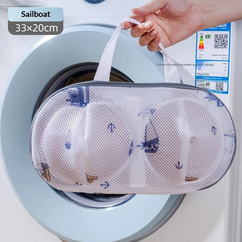 A white mesh laundry bag with blue embroidery is placed inside a washing machine drum.