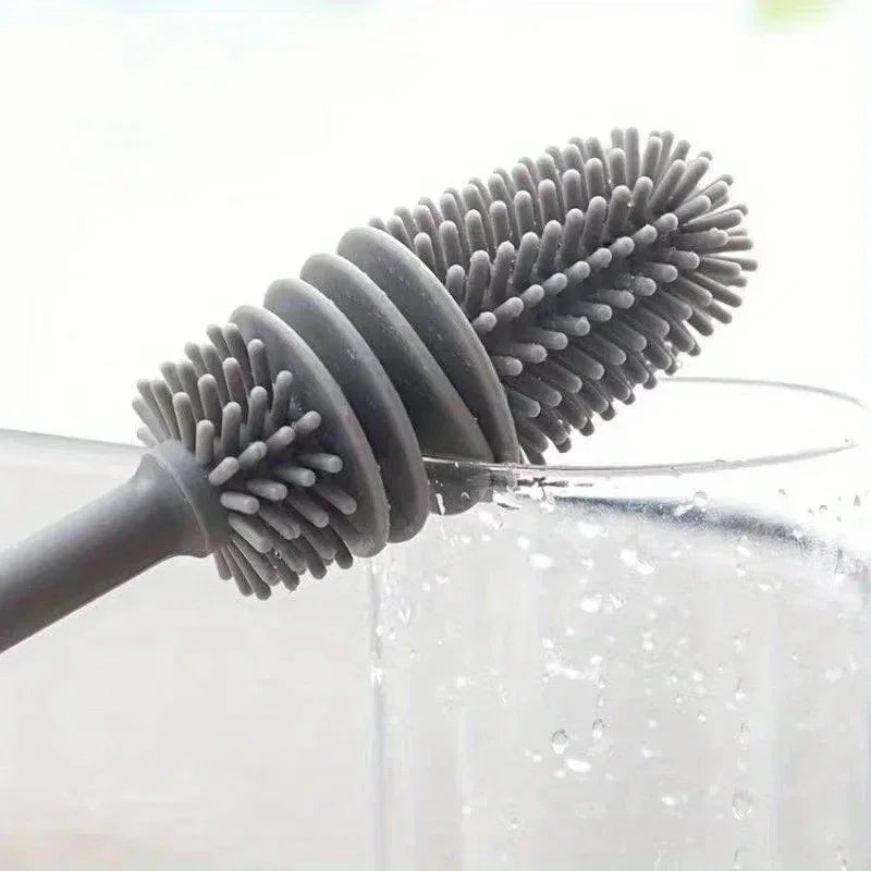 A silicone bottle brush with a long handle is shown dipping into clear water for cleaning.