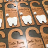 A collection of wooden tooth fairy door hangers for kids, featuring various tooth shapes and names.