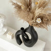 A black ceramic vase with an organic, sculptural shape holds dried beige floral arrangements.