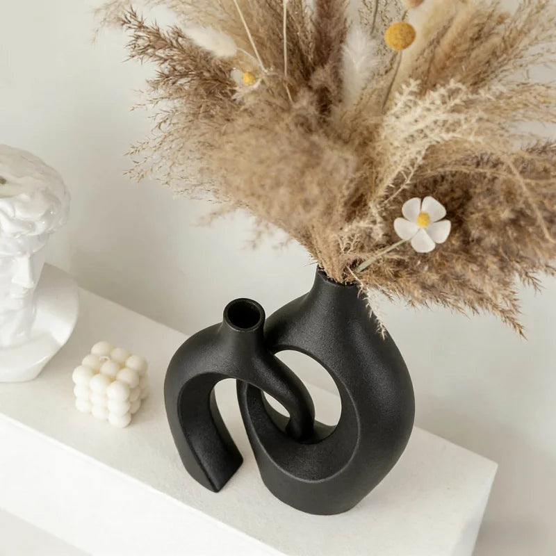 A black ceramic vase with an organic, sculptural shape holds dried beige floral arrangements.