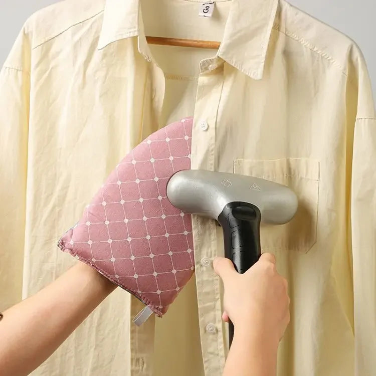A person is using a handheld ironing tool with a black handle and silver body, alongside a pink ironing board cover, while we