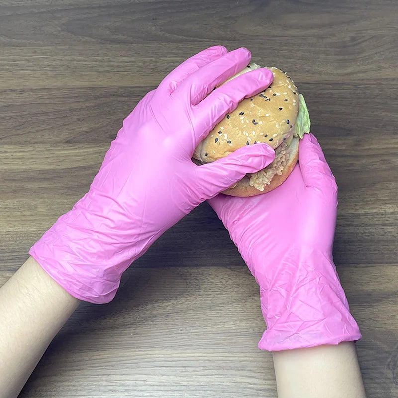 A hand wearing a pink disposable nitrile glove is holding a hamburger bun with fillings.