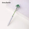 A silver pen with a green fluorite crystal attached, resting on a white surface.
