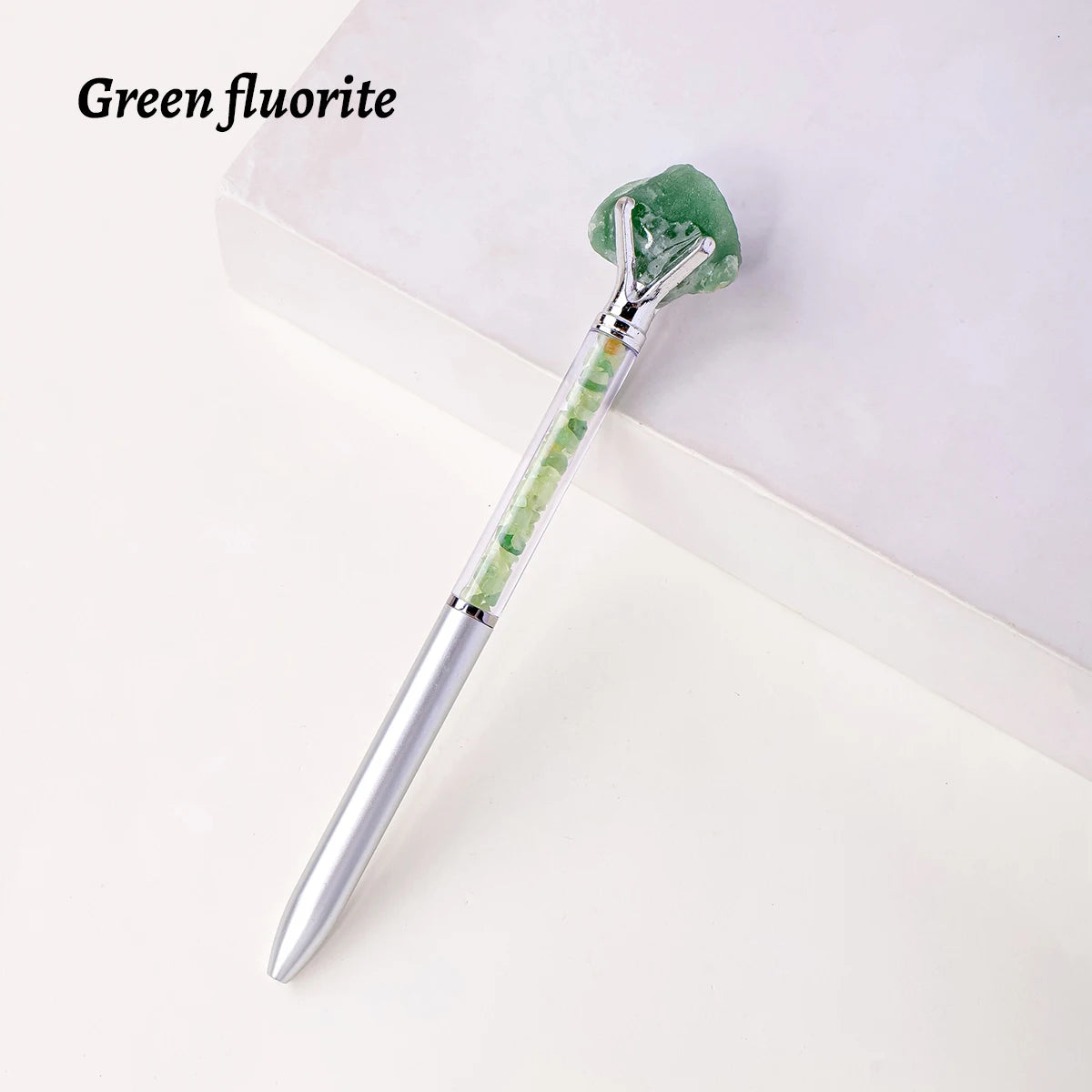 A silver pen with a green fluorite crystal attached, resting on a white surface.