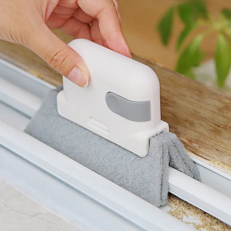 A hand is using a white groove cleaning brush to clean dirt from a window track.