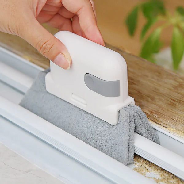 A hand is using a white groove cleaning brush to clean dirt from a window track.